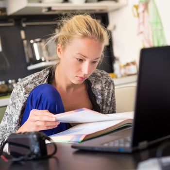 Female freelancer in her casual home clothing working remotly from her dining table in the morning. Home kitchen in the background.