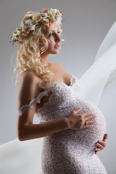 Young pregnant woman in a white dress with a garland made of flowers