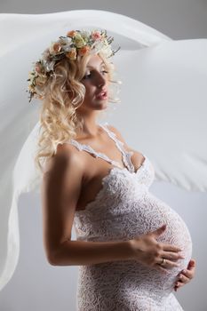 Young pregnant woman in a white dress with a garland made of flowers