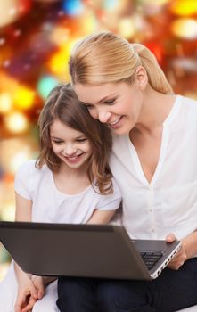 family, childhood, holidays, technology and people concept - smiling mother and little girl with laptop computer over red lights background