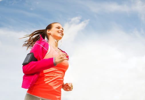 fitness, sport and lifestyle concept - smiling young woman with earphones running outdoors