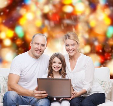 family, childhood, holidays, technology and people concept - smiling family with laptop computer over red lights background