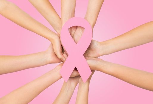 healthcare, people and medicine concept - close up of women hands with paper cancer awareness symbol over pink background