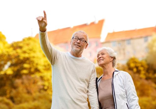 family, age, tourism, travel and people concept - senior couple pointing finger in city park