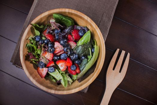 Delicious fresh salad on wooden bowl with berries and mixed greeens