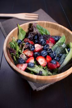 Healthy fresh salad on wooden bowl with berries and spinach