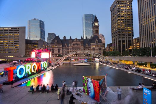 TORONTO,CANADA-JULY 9,2015: Panoramic view of the new Toronto sign in Nathan Phillips Square, host of PanaMania, a contant party celebrating the PanAm games. Old City Hall and downtown buildings in the back. 