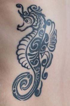 A tattoo of a black tribal style seahorse on a woman's ribs.