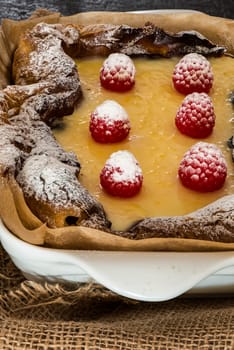 eclair cake in casserole dish with raspberry on wood table