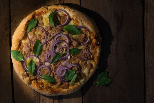 top view of a round tuna pizza with onion rings on a dark wooden table