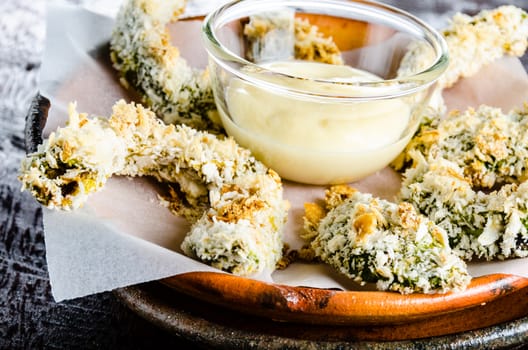 breaded baked avocado pieces served with a mayonnaise sauce on clay plate and wood background