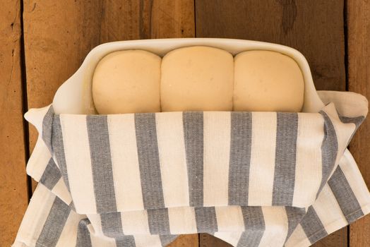 baking dish with yeast dough in the form of an bun half covered with a kitchen towel