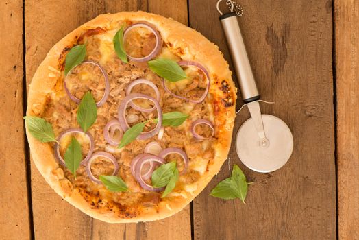 top view a round tuna pizza with onion rings on a wooden table and a pizza cutter