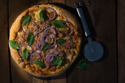 top view a round tuna pizza with onion rings on a dark wooden table and a pizza cutter