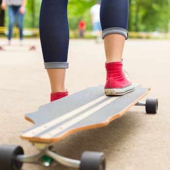 Girl wearing black boots and stockings practicing long board riding in skateboarding park. Active urban life. Urban subculture.