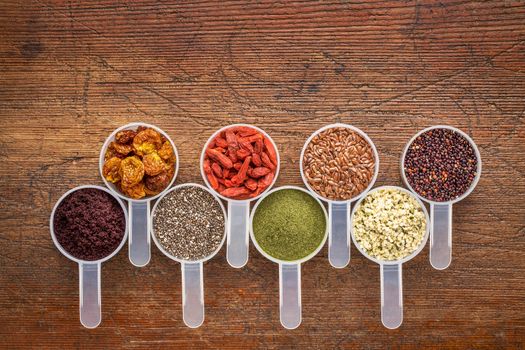 superfood abstract (wheatgrass, acai berry, goji berry, flax seed,chia seed,goldenberry, hemp seed, quinoa grain) - top view of measuring scoop against rustic wood with a copy space