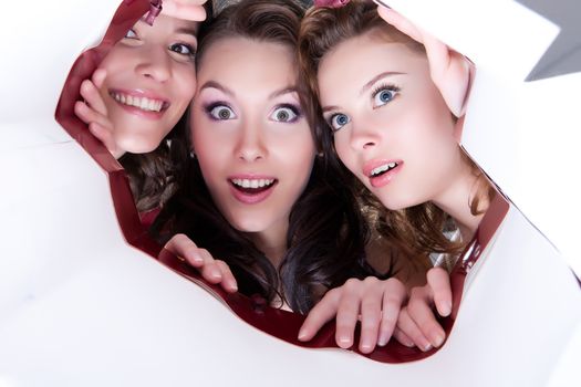 Three young smiling women looking into the paper shopping bag