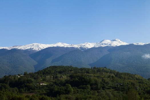 Mountains are covered with snow and the wood and surrounded with clouds