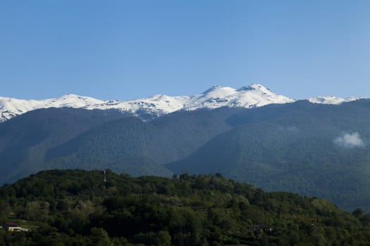 Mountains are covered with snow and the wood and surrounded with clouds