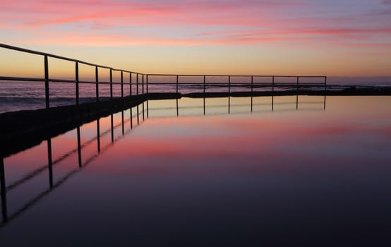 Sunrise views across the Wpmbarra ocean rock pool with reflections.  Wombarra NSW  Australia