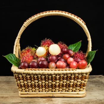 fresh fruit red grapes and rambutan in basket on wood background .