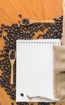 White notebook for your text with sackcloth and coffee beans on wooden spoon.