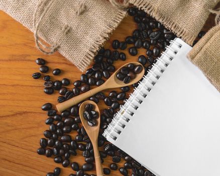 White notebook for your text with sackcloth and coffee beans on wooden spoon.