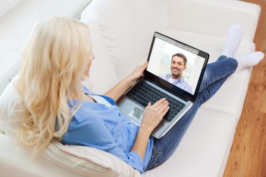 home, technology, communication and people concept - smiling woman sitting on couch and chatting with laptop computer at home