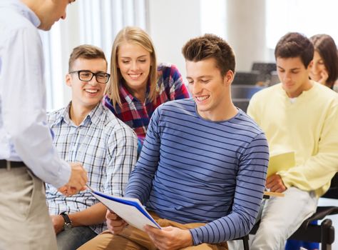 education, high school, teamwork and people concept - group of smiling students with notebooks and teacher talking in classroom