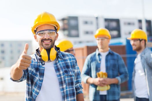 business, building, teamwork, gesture and people concept - group of smiling builders in hardhats showing thumbs up outdoors