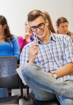 education, high school, teamwork and people concept - group of smiling students with paper and pen sitting in lecture hall and writing