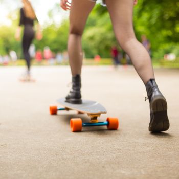 Teenage girl wearing black boots and stockings practicing long board riding outdoors in skateboarding park. Active urban life. Urban subculture. Motion blured. Focus on the floor for copy space.