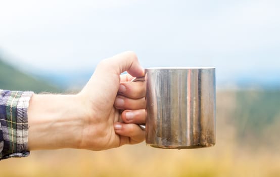 Metal touristic tea cup in man hand on outdoor background