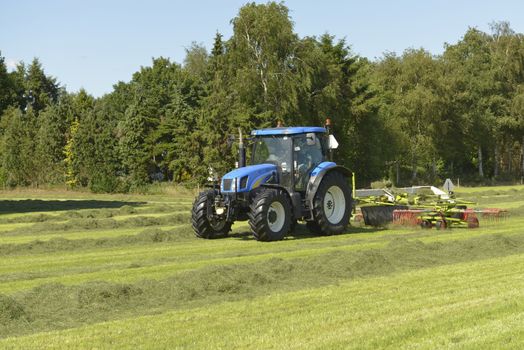 Agriculture, the kidding of shaken grass with blue tractor with kidder
