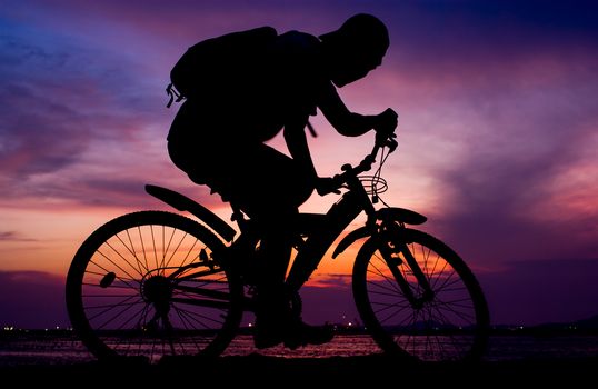 Silhouette of backpacker ride mountain bike on bridge beside sea with sunset sky background