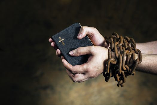 Hands holding a bible tied together with an old rusty chain.