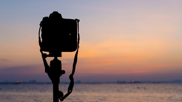 Silhouette of DSLR camera at sea with sunset sky