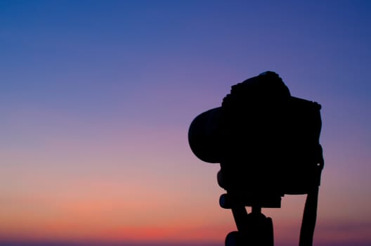 Silhouette of DSLR camera at sea with sunset sky