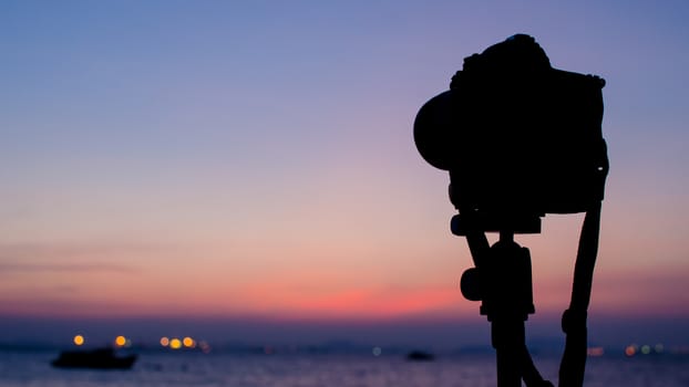 Silhouette of DSLR camera at sea with sunset sky