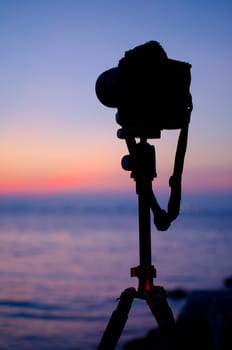 Silhouette of DSLR camera at sea with sunset sky