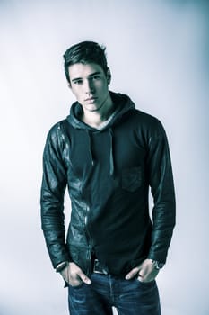 Handsome young man in black hoodie sweater on light background, looking at camera. Studio shot