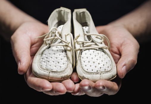 Man holding old worn white baby shoes in his hands.