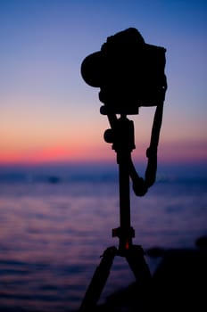 Silhouette of DSLR camera at sea with sunset sky