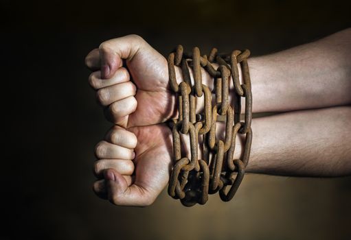 Hands of a man with a rusty chain around the wrists.