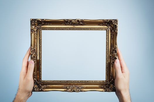 Man holding an antique look golden picture frame in his hands.
