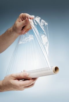 Man holding a roll of plastic film, typically used for sealing food items.