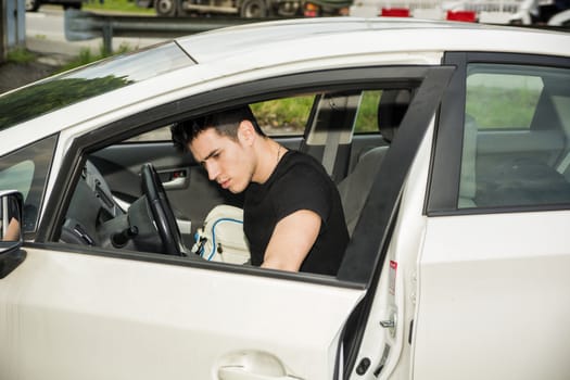 Young attractive man getting out of white car, opening the door