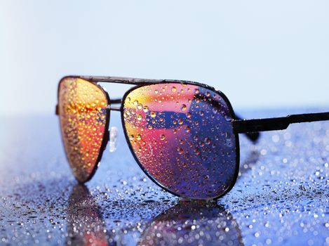 Wet sunglasses on a wet reflective surface.
