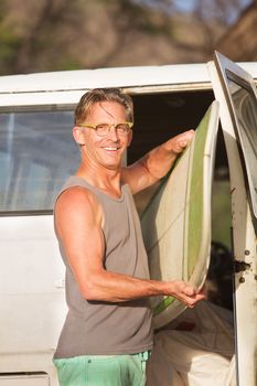 Smiling person with eyeglasses taking a surfboard from his van