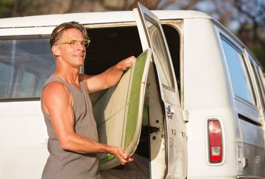 Single handsome man removing surfboard from of his van